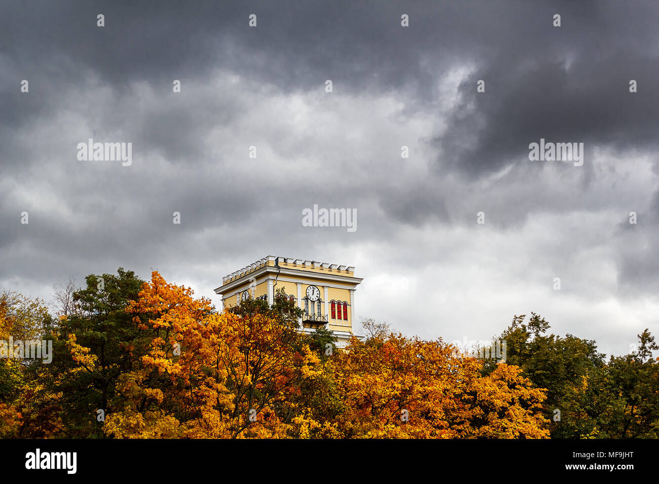 A tall building with a clock against an approaching storm in the sky. An ancient building among the foliage and the approaching thunderstorm Stock Photo