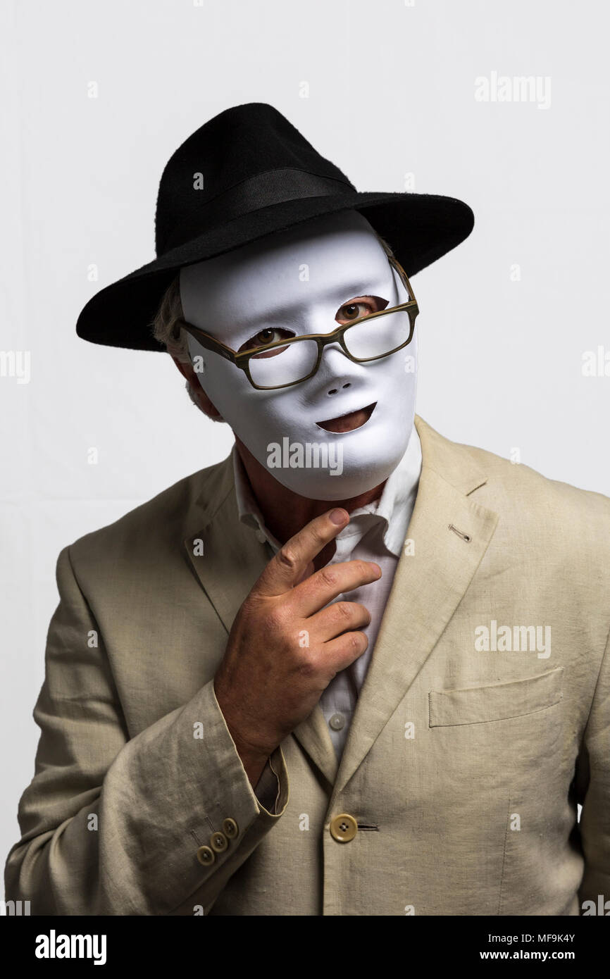 Man wearing white face mask, black hat, and linen jacket against white background Stock Photo