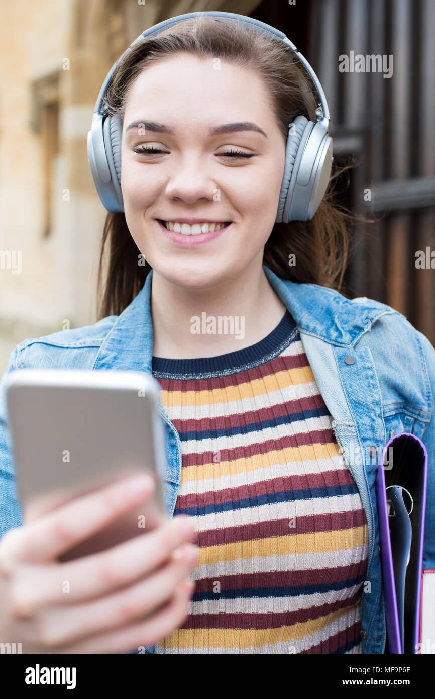 Female Student Outside College Building Streaming Music From Mobile Phone Stock Photo