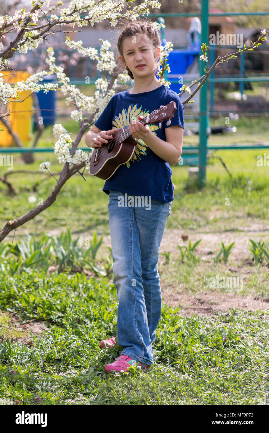 A little girl playing ukulele in the garden. Stock Photo