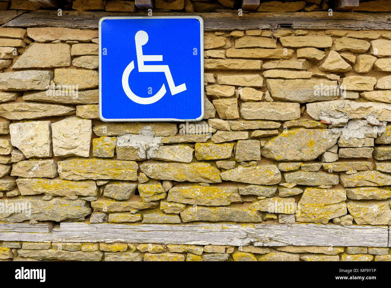 Traffic sign indicating parking for persons with disabilities hanging on rough stone wall, Disabled Access Sign, Handicap Accessible Sign Stock Photo
