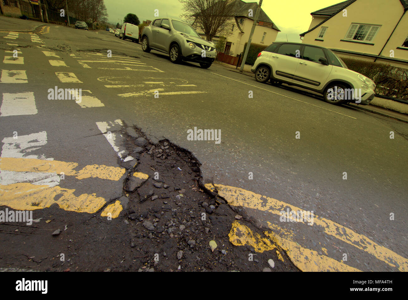 pot holes damaged road  car cars on street with  double yellow lines no entry markings Stock Photo