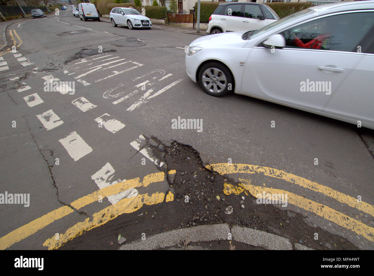 pot holes damaged road  car cars on street with  double yellow lines no entry markings Stock Photo