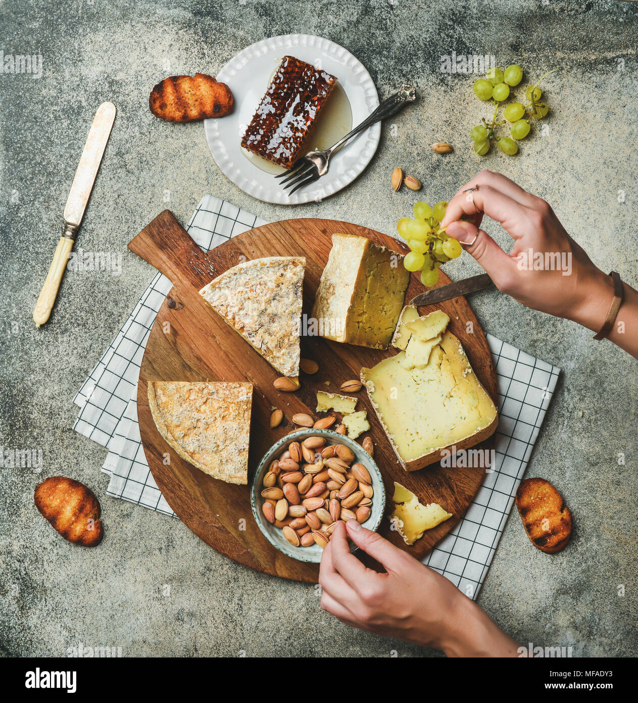 Cheese platter with female hands reaching to food Stock Photo