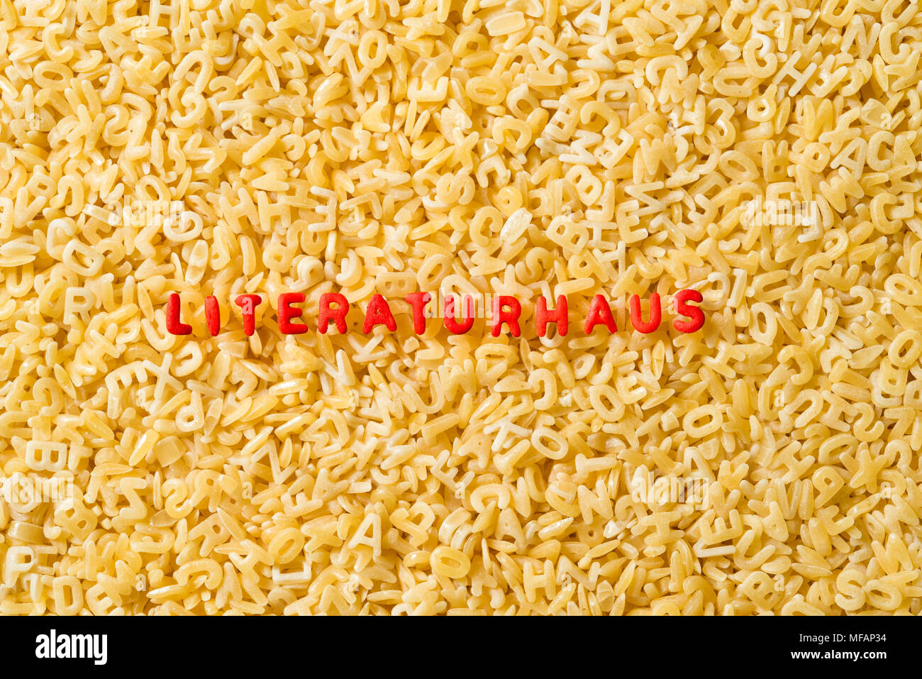The german word 'LITERATURHAUS' is spelled with red colored abc pasta letters. The background is made from uncooked natural abc pasta letters. Stock Photo