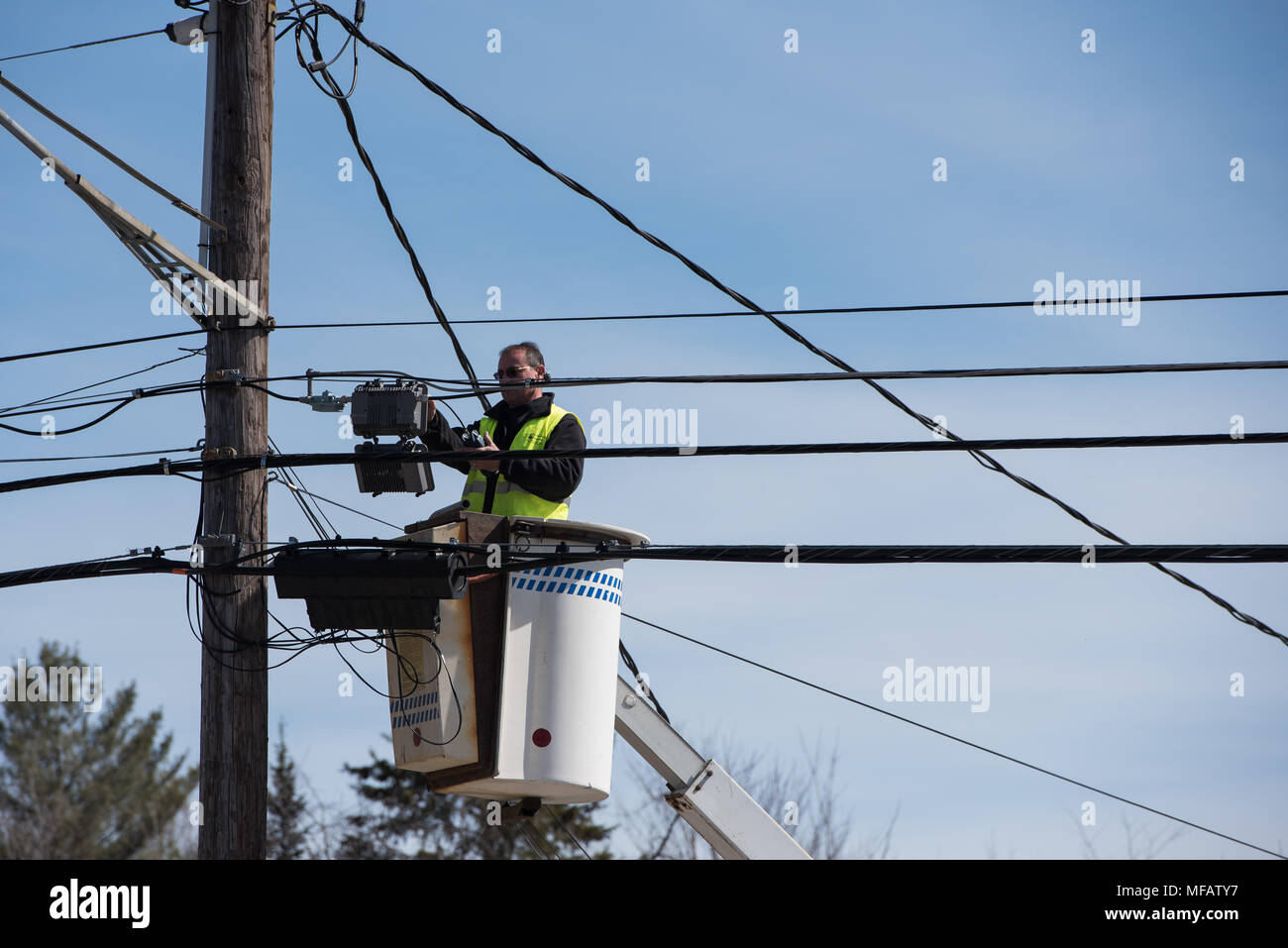 Man working on wires while standing in an aerial work platform, or lift bucket or bucket truck with a deep blue background. Stock Photo