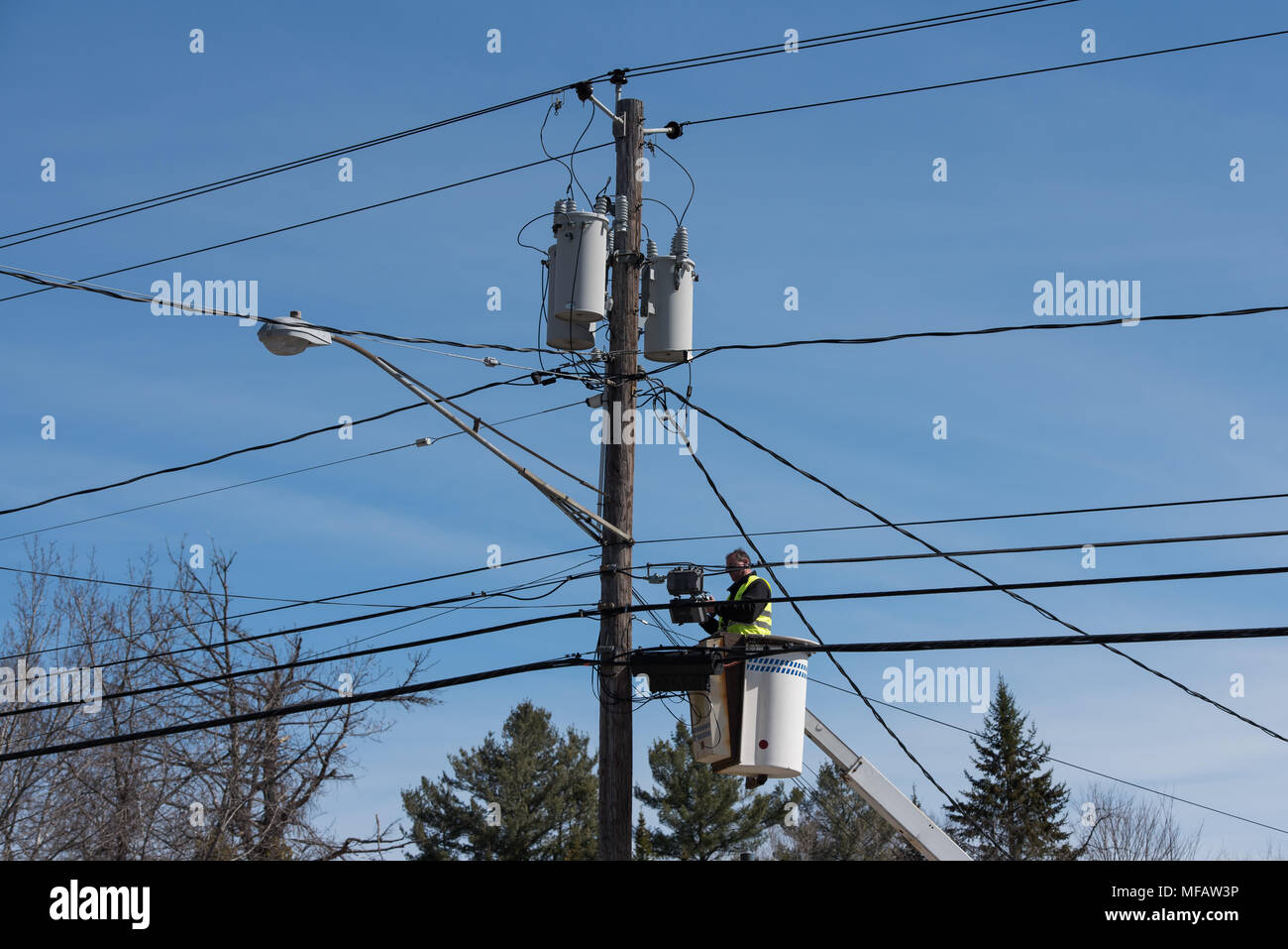 Man working on wires while standing in an aerial work platform, or lift bucket or bucket truck with a deep blue background. Stock Photo