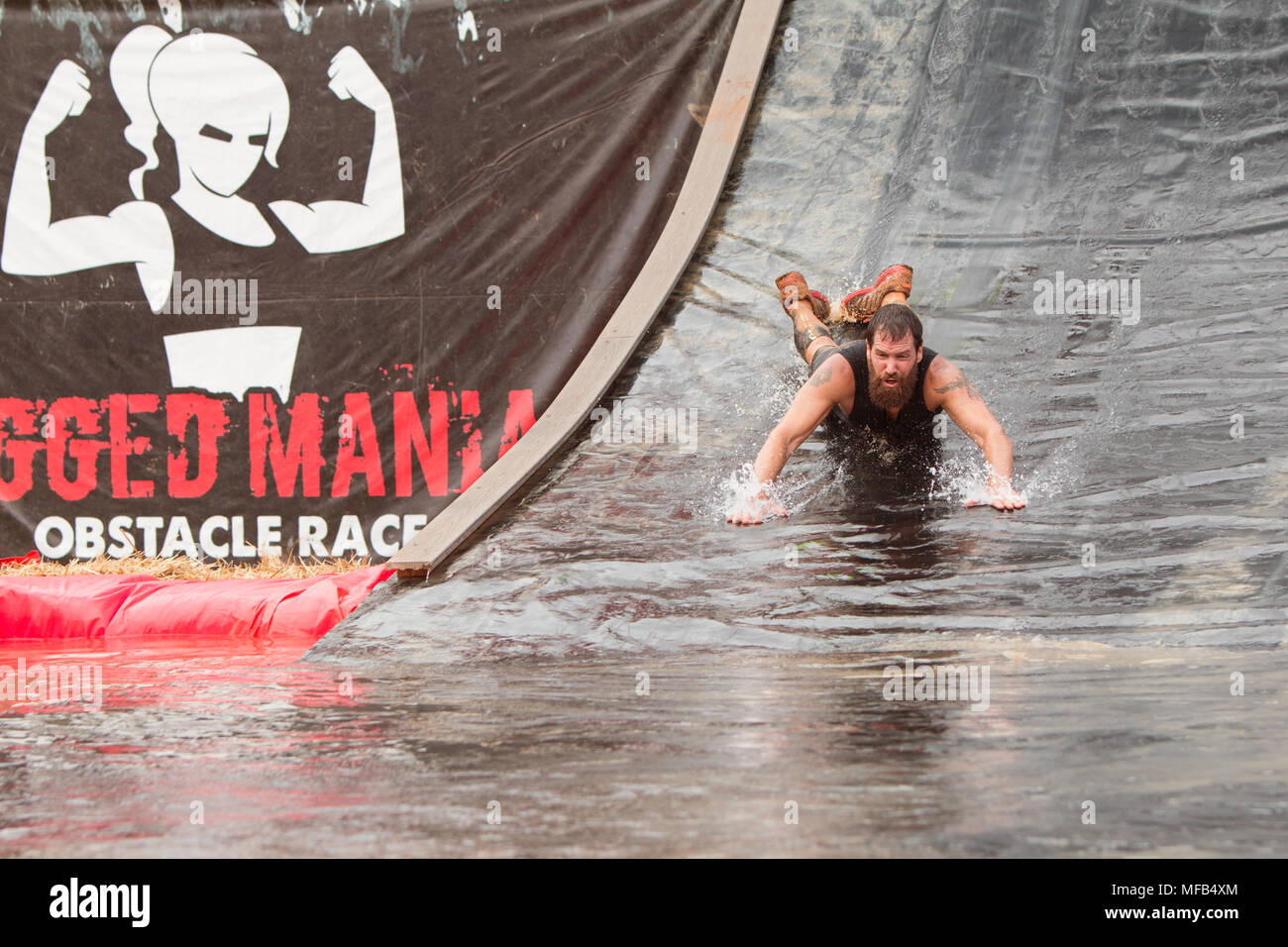 A man goes down a water slide headfirst into a pool of water as he competes in the Rugged Maniac Obstacle Course on August 22, 2015 in Conyers, GA. Stock Photo