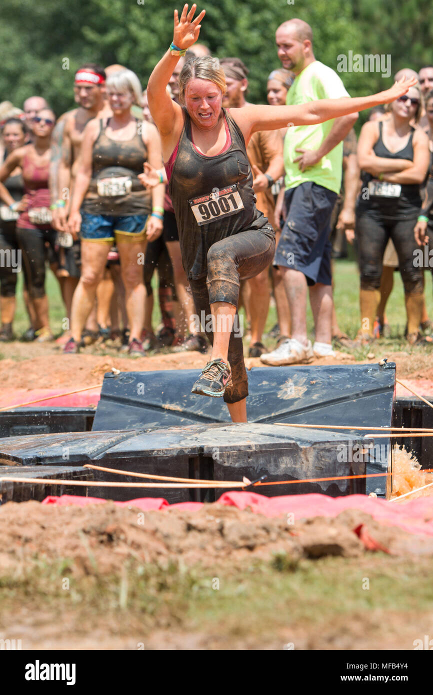 A young woman tries to run across platforms floating in a pit of muddy water at the Rugged Maniac Obstacle Course on August 22, 2015 in Conyers, GA. Stock Photo