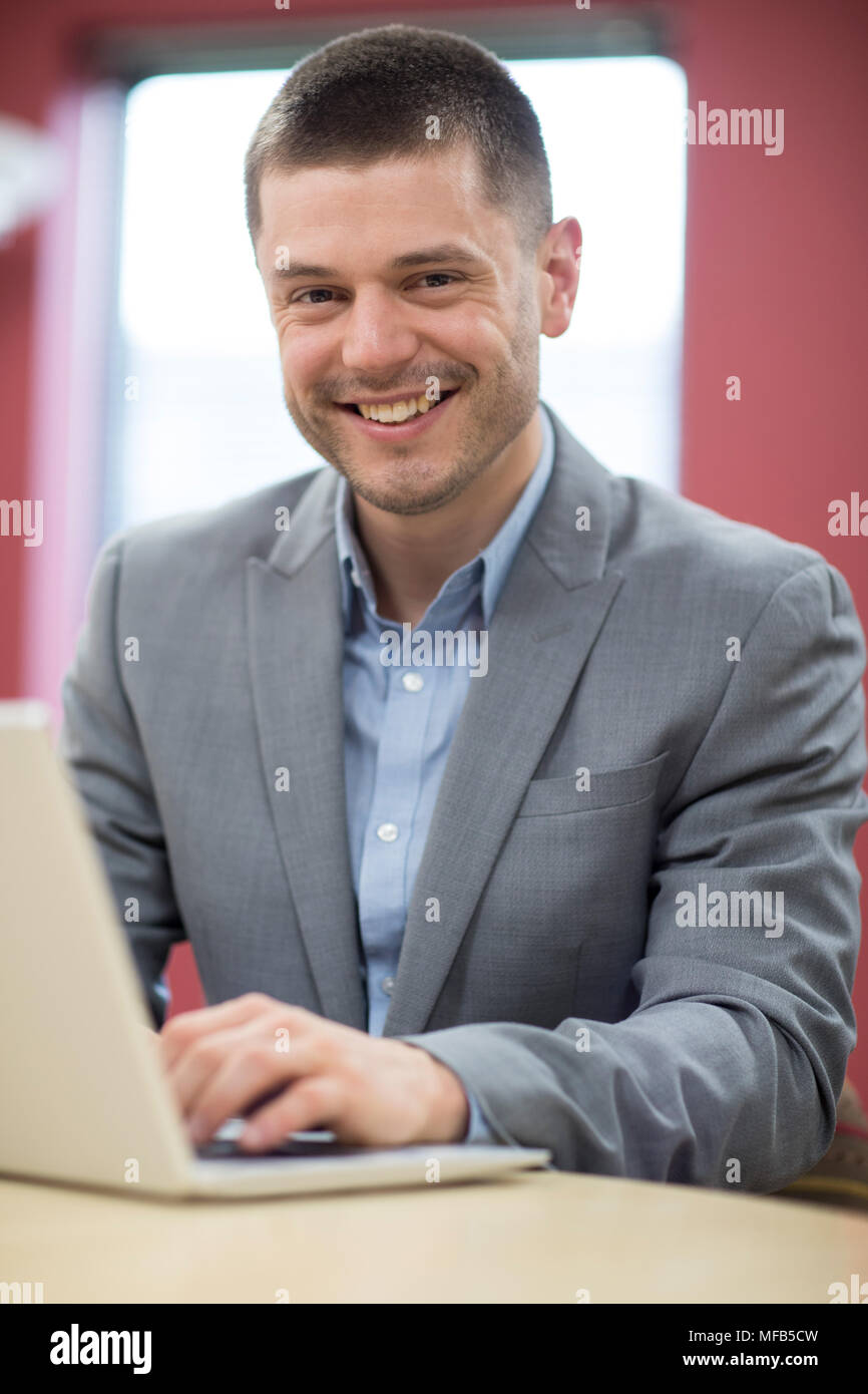 Portrait Of Businessman Sitting At Desk In Office Using Laptop Stock Photo
