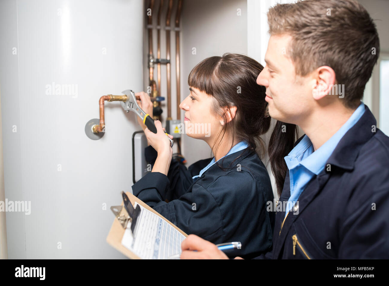 Female Trainee Plumber Working On Central Heating Boiler With Male Engineer Stock Photo