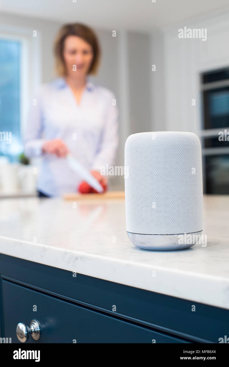 Woman Working In Kitchen With Smart Speaker In Foreground Stock Photo