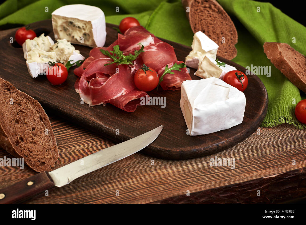 Cheese, prosciutto, bread, vegetables and spices on wooden board on