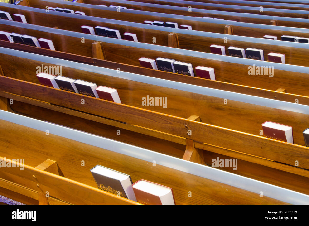 Rows of pews in a church have book shelves holding Bibles and pews behind the seats. Stock Photo