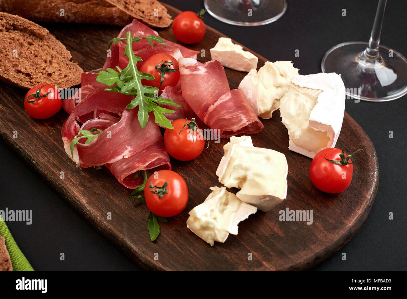 Cheese, prosciutto, bread, vegetables and spices on wooden board on