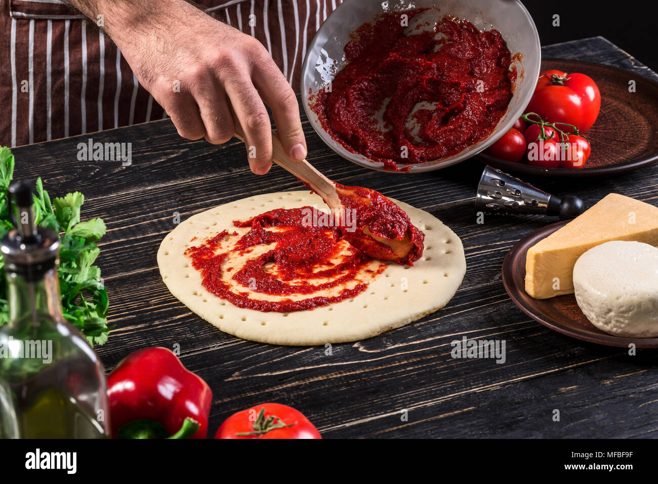 A male hand spreading tomato puree on a pizza base with spoon on an old