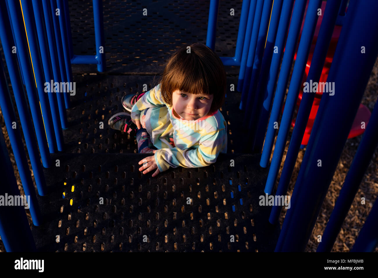 A 3-year old girl on a playground equipment on a summer day. Stock Photo