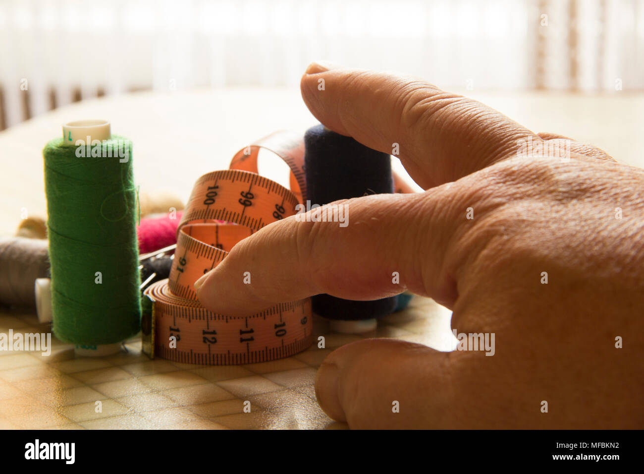 The tailor's fingers hold a multicolored thread and a meter Stock Photo ...