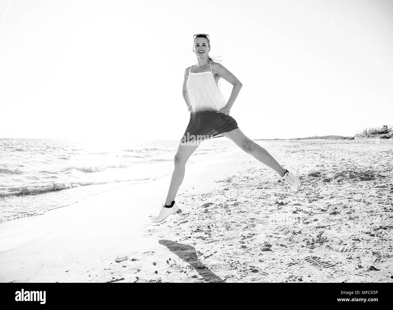 wonderfully cheerful mood. Full length portrait of young woman in dress on the beach in the evening jumping Stock Photo