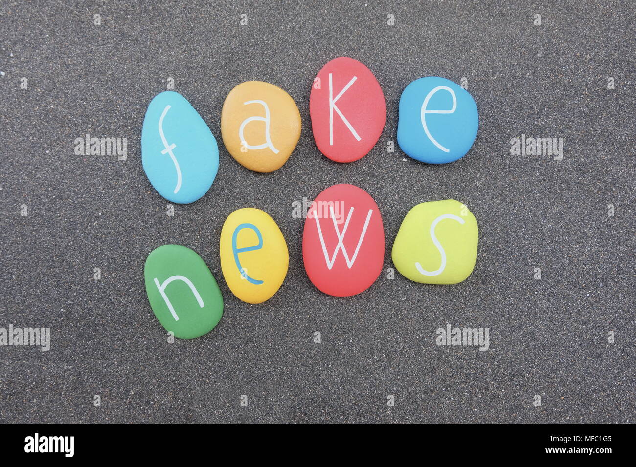 Fake news text with multicolored stones over black volcanic sand Stock Photo