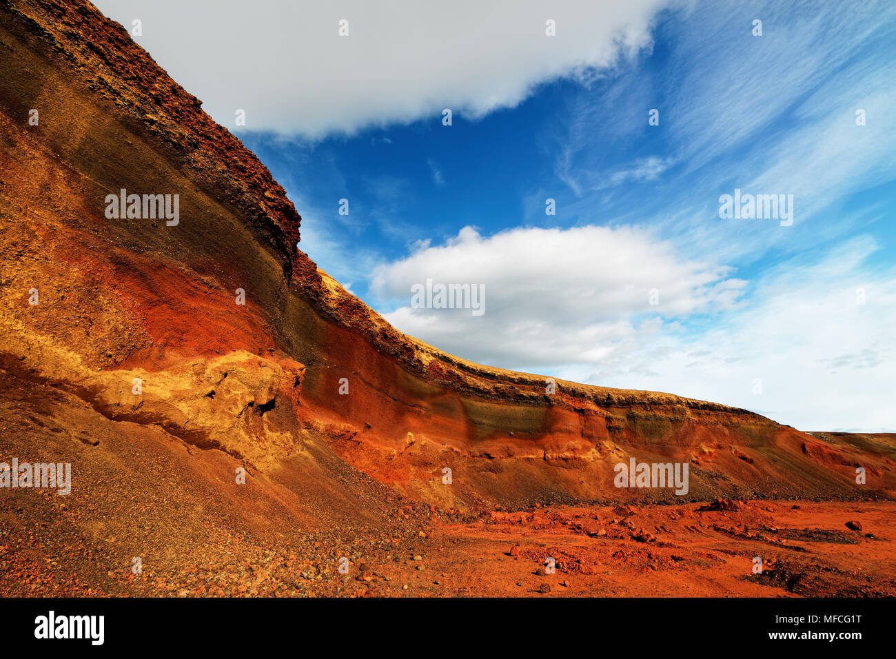 Colorful deposits of volcanic ash in reds and yellows against a green hill, above blue sky with clouds - Location: Iceland, Golden Circle Stock Photo