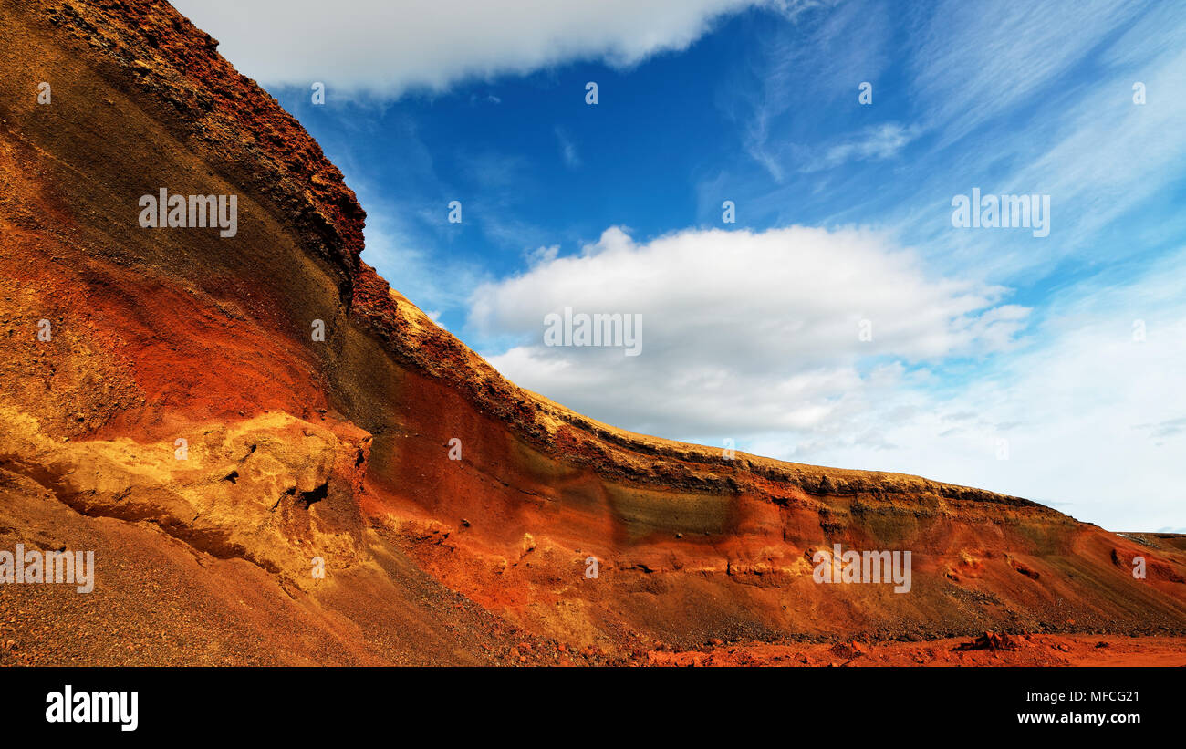 Colorful deposits of volcanic ash in reds and yellows against a green hill, above blue sky with clouds - Location: Iceland, Golden Circle Stock Photo