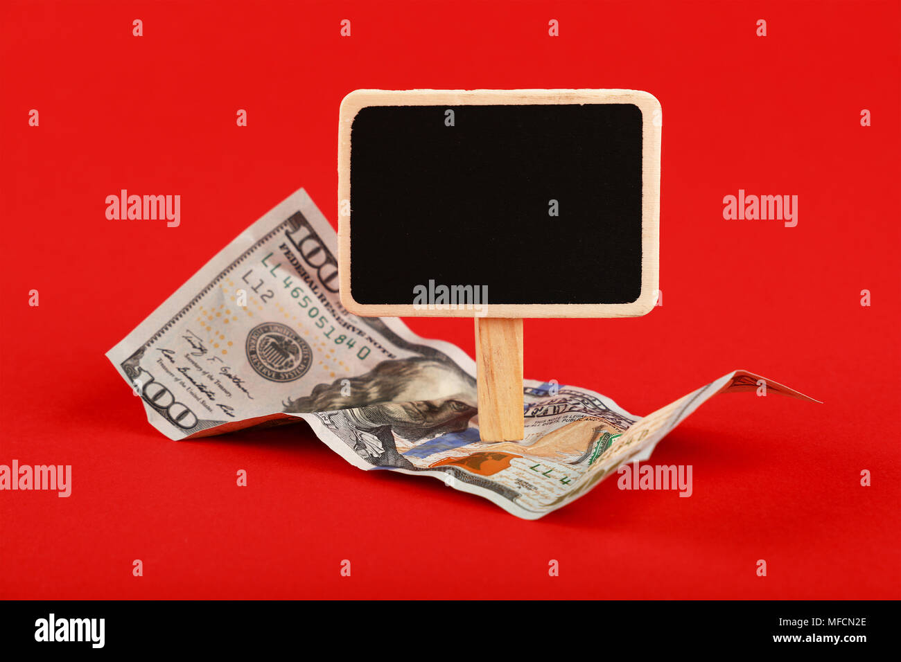 Close up one hundred US dollar paper currency banknote and blank chalk blackboard sign with copy space over red background, high angle view Stock Photo