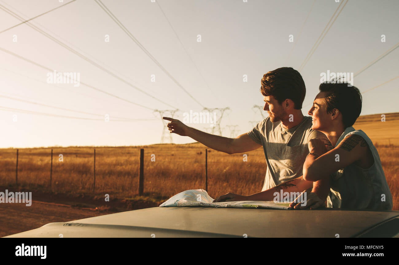 Couple using a map for navigation while on a road trip in country side. Man pointing in the direction of the road while using a map to navigate. Stock Photo