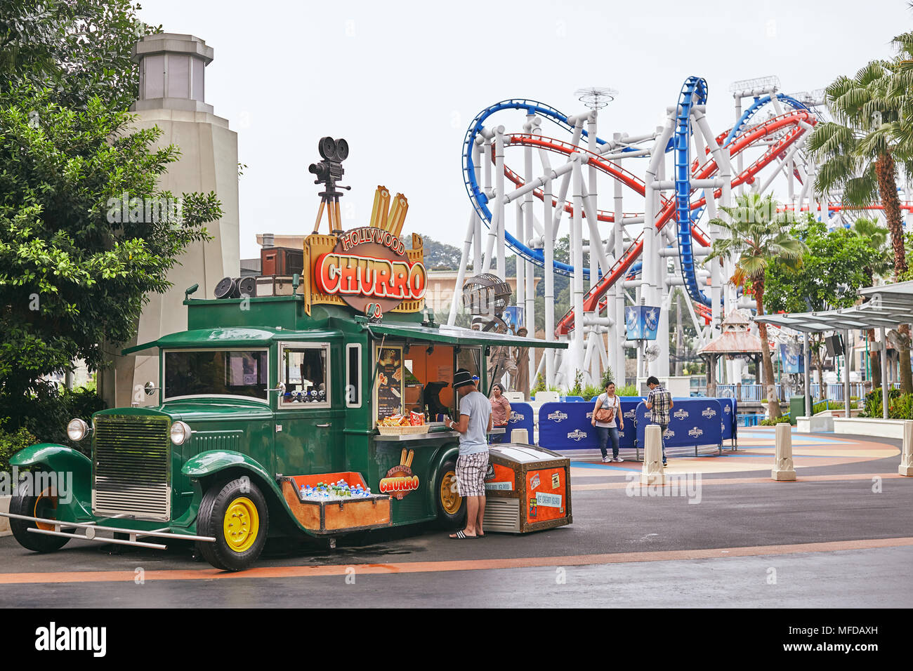 A man buying some food and drink at the big green truck selling snacks, food and drink in the street at universal studio Singapore with rollercoaster  Stock Photo