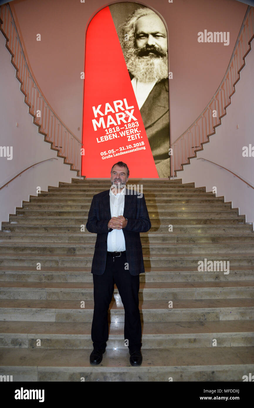 25 April 2018, Germany, Trier: Marcus Reuter, head of the Rheinische Landesmuseum Trier, speaking to media representatives in front of a poster advertising the large Karl Marx exhibition. According to its organizers, Rhineland-Palatinate's state exhibition "Karl Marx 1818 - 1883. Life. Work. Times" ist the first ever historico-cultural exhibition on the thinker. It can be seen at the Rheinische Landesmuseum Trier and at the Simeonstift Trier city museum. Photo: Harald Tittel/dpa Stock Photo