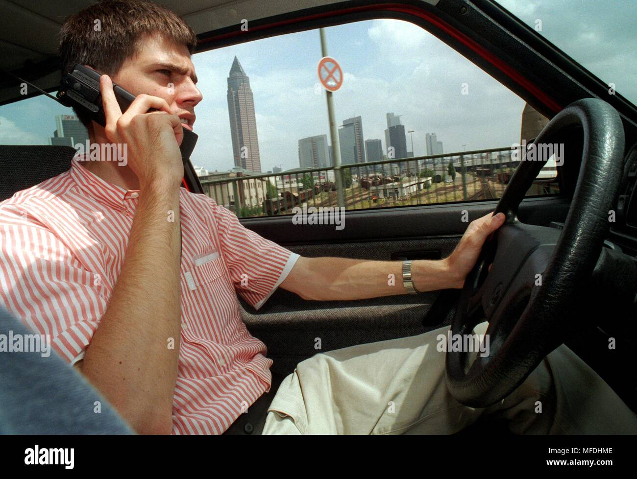 A car driver telephones on 15.7.96 during a drive in the Frankfurt city center (in the background the Messeturm and Hochhauser of the banks). The Chairman of the Bonn Transport Committee, Dionys Jobst, had spoken out in favor of a ban on telephoning during the journey, as in Switzerland, Italy or Sweden. But for the time being, everything remains the same - road users in Germany may also sit behind the wheel with mobile phones. | usage worldwide Stock Photo