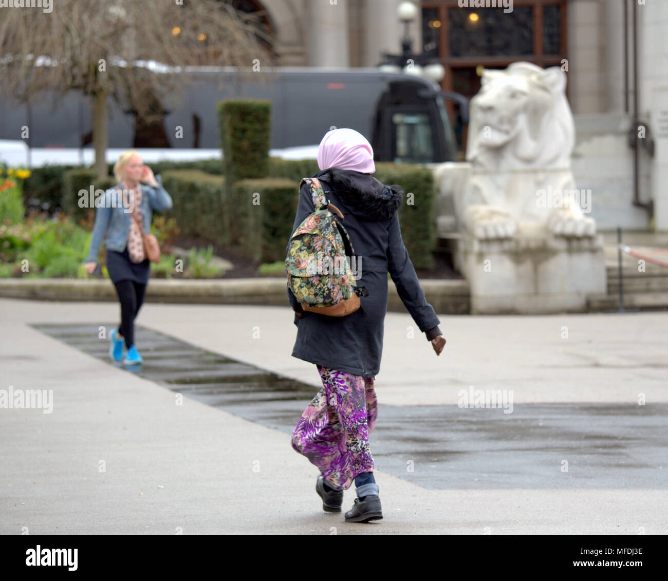 Glasgow, Scotland, UK 25th April. UK Weather: Muslim woman hijab white blonde woman on phone walking in front of George Square cenotaph colonial royal   lion statue locals and tourists inn  Sunshine and showers as the locals and tourists enjoy the beginning of summer. Gerard Ferry/Alamy news Stock Photo