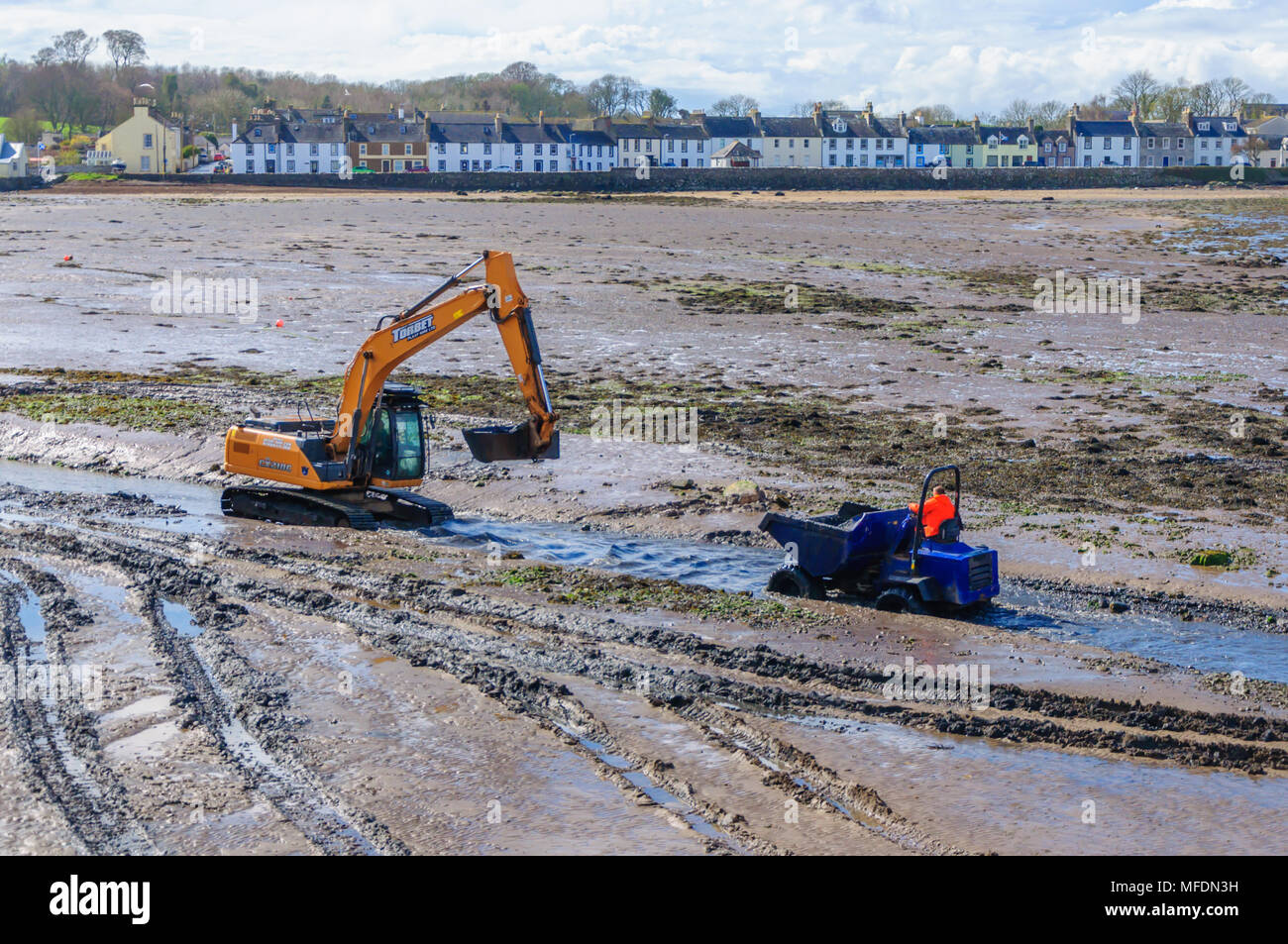 Garlieston, Dumfries & Galloway, Scotland, UK. 25th April, 2018. UK Weather. Mechanical plant on the beach at low tide to clear rocks, boulders and the build up of silt to help clear the water way around the harbour on a sunny afternoon. Credit: Skully/Alamy Live News Stock Photo