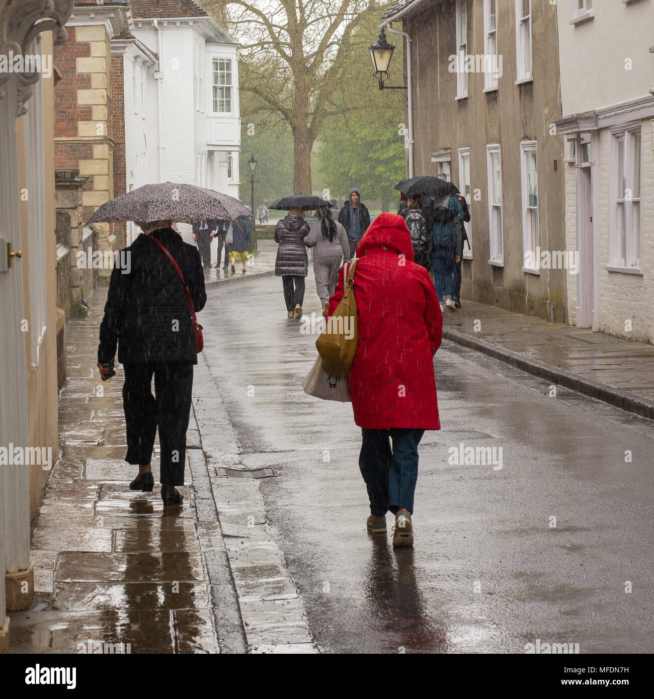 People walking with umbrellas during a heavy April rain shower in the entrance to Cathedral Close, Salisbury, Wiltshire, UK Stock Photo