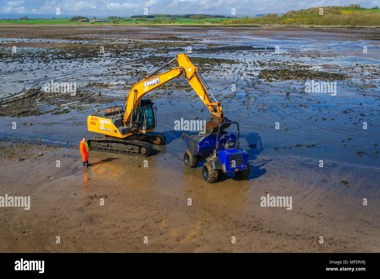 Garlieston, Dumfries & Galloway, Scotland, UK. 25th April, 2018. UK Weather. Mechanical plant on the beach at low tide to clear rocks, boulders and the build up of silt to help clear the water way around the harbour on a sunny afternoon. Credit: Skully/Alamy Live News Stock Photo