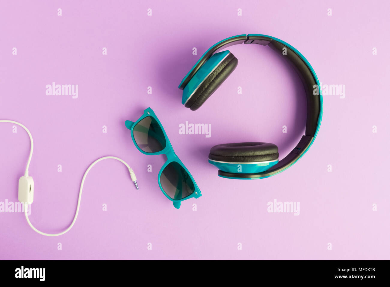 Turquoise headphones and sunglasses with cable isolated on pastel purple background flat lay. Stock Photo