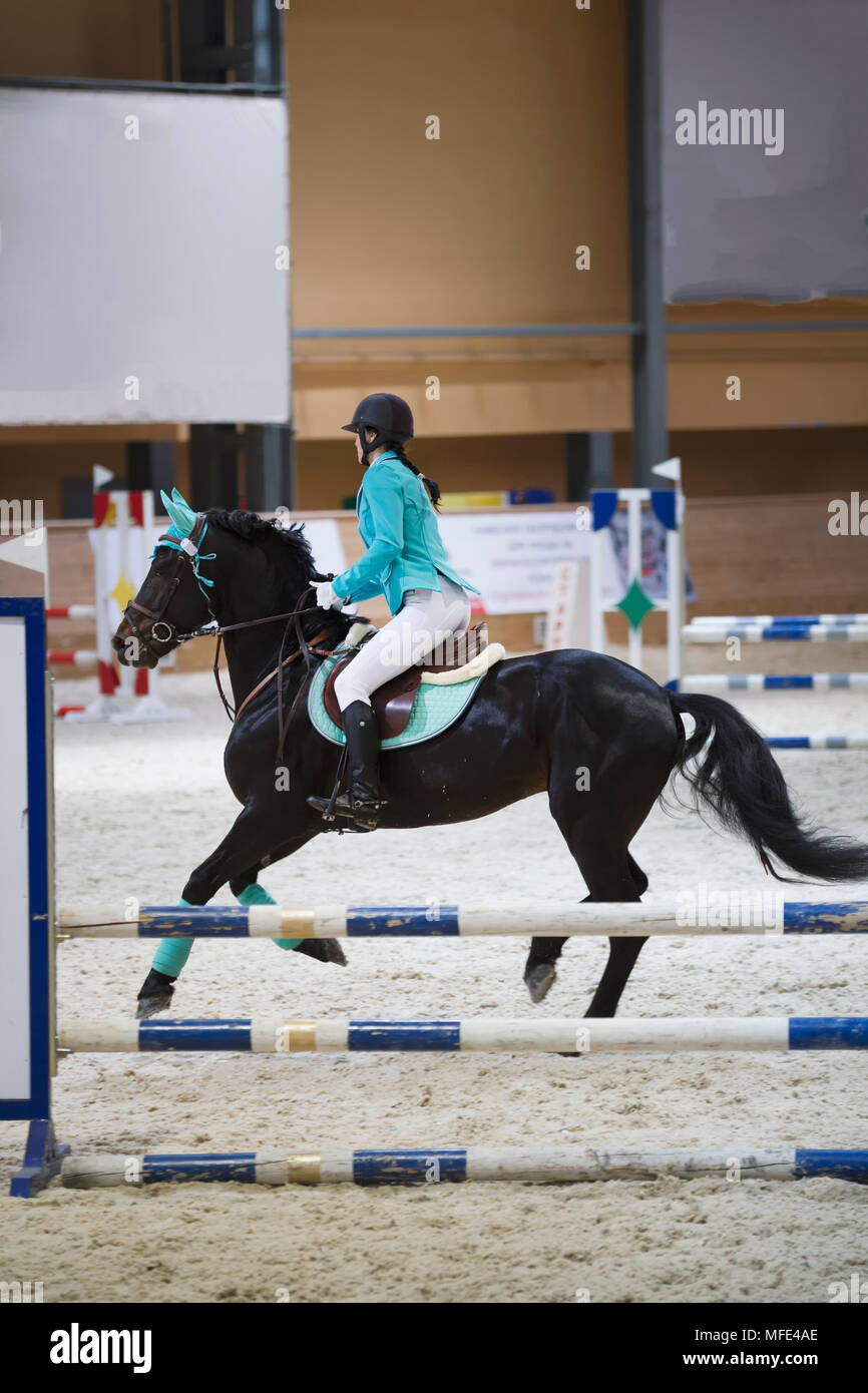Slim young woman on the black horse galloping at show jumping competition Stock Photo