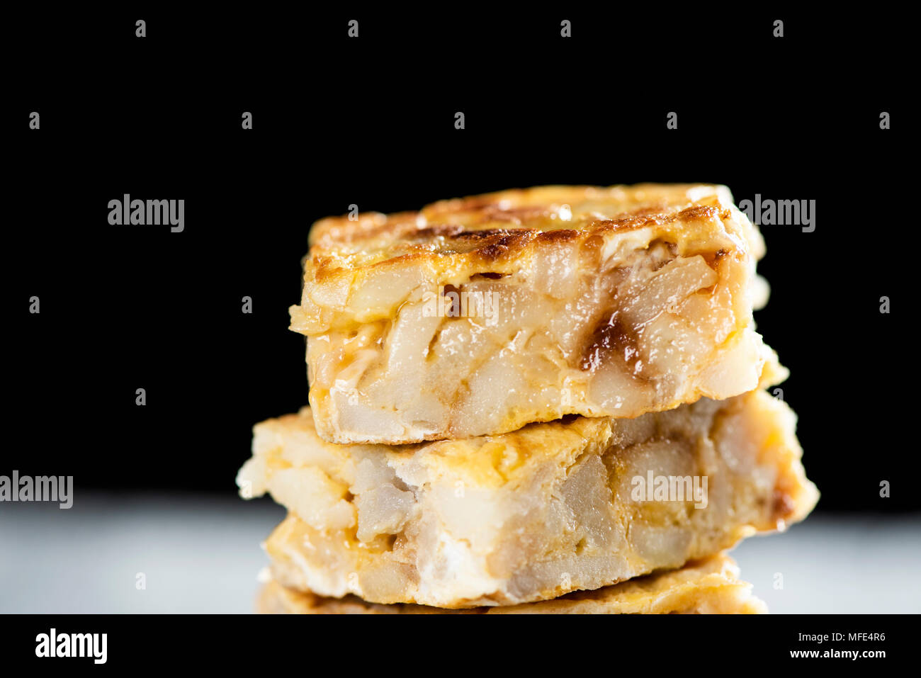closeup of some pieces of typical tortilla de patatas, spanish omelet, on a rustic wooden table, against a black background Stock Photo
