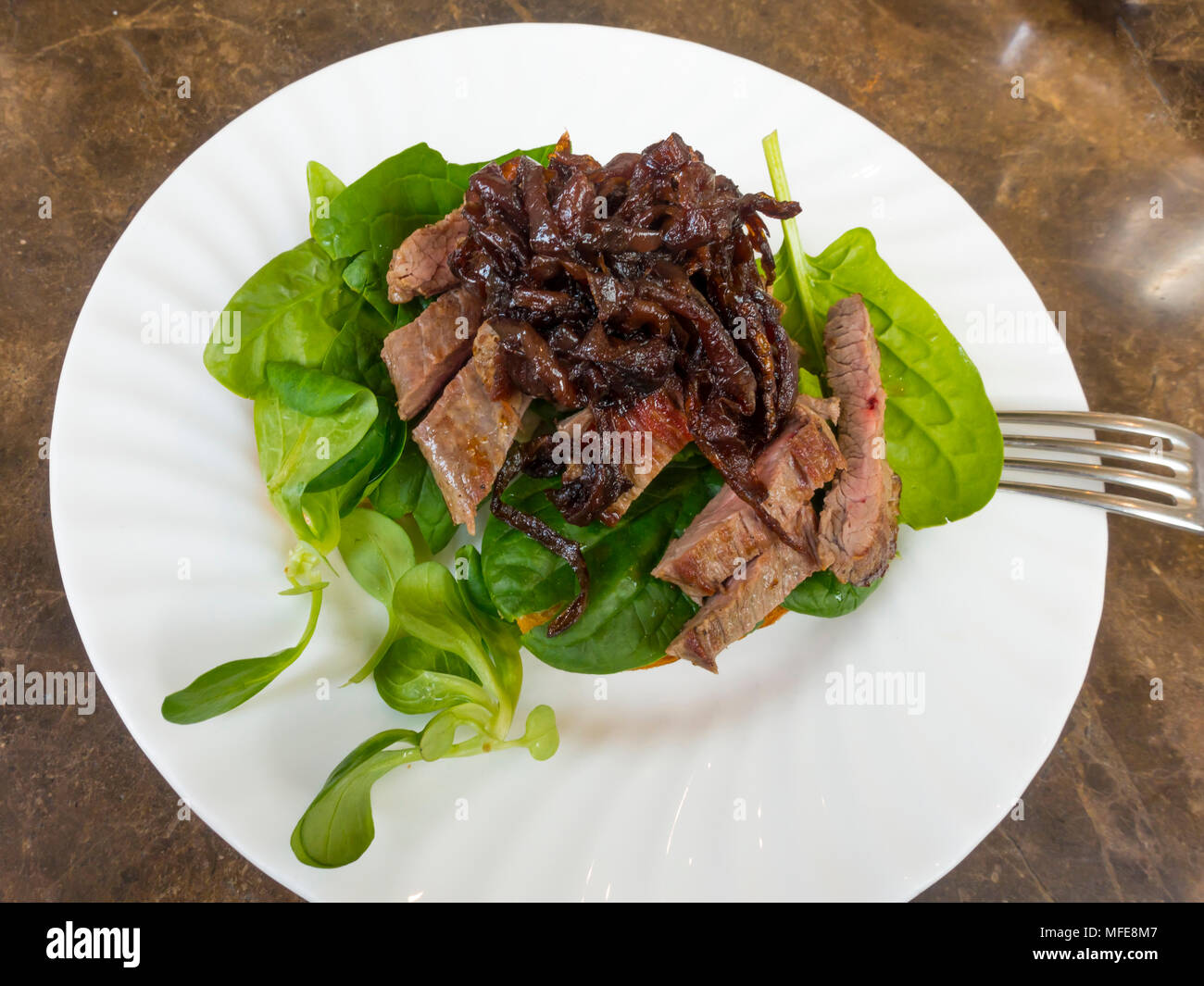 Lunchtime snack Steak open sandwich served with caramelised red onion, horseradish mayonnaise and baby leaf spinach Stock Photo