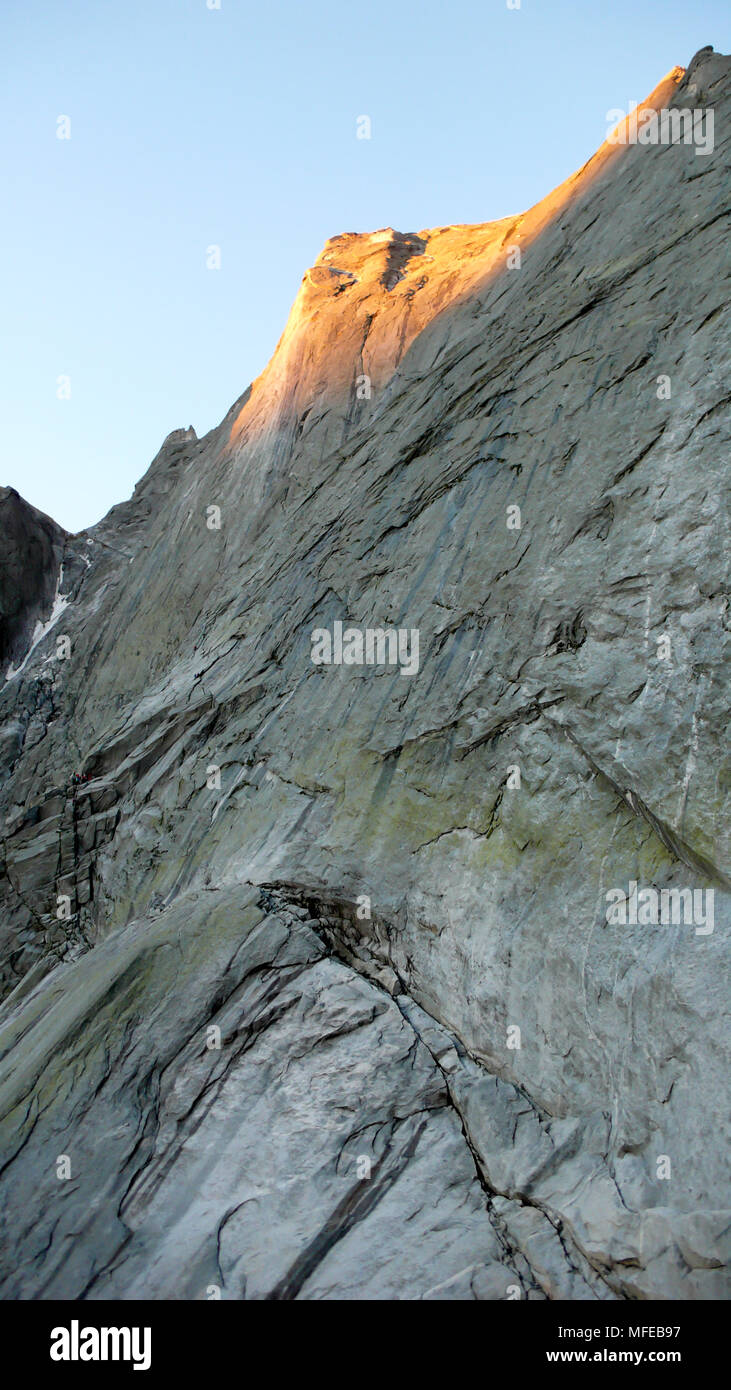 view of the classic northeast face of Pizzo Badile and its many climbing routes with one climber approaching the famous Via Cassin Stock Photo