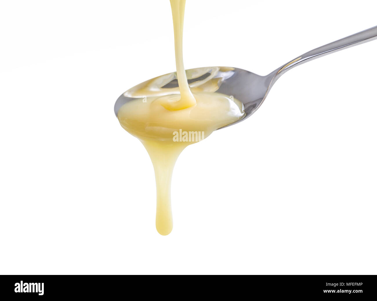 closeup pouring condensed milk with teaspoon on white background Stock