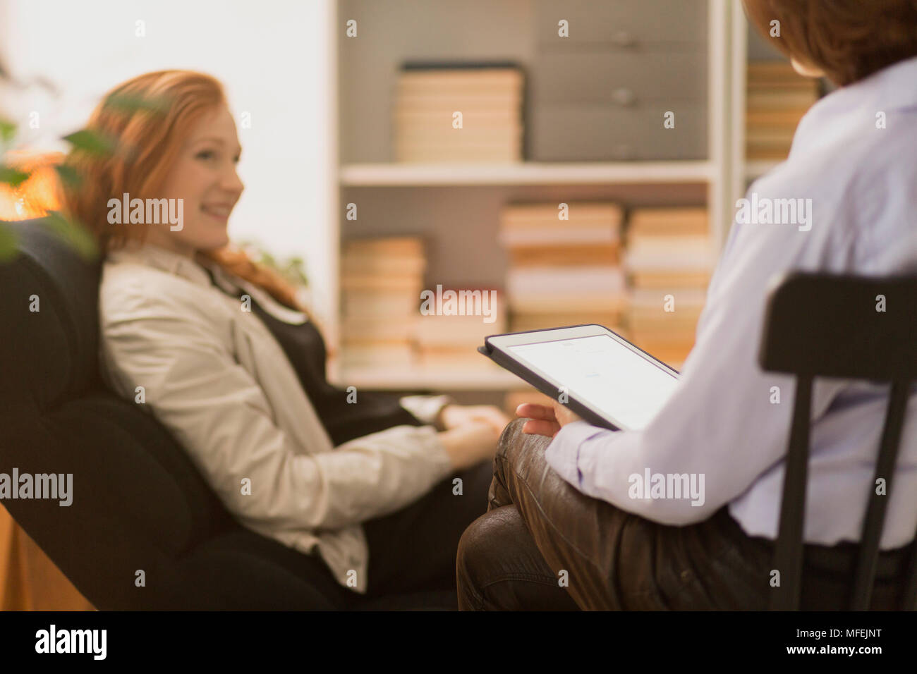 Woman sitting in a chair and talking to a therapist during psychotherapy Stock Photo