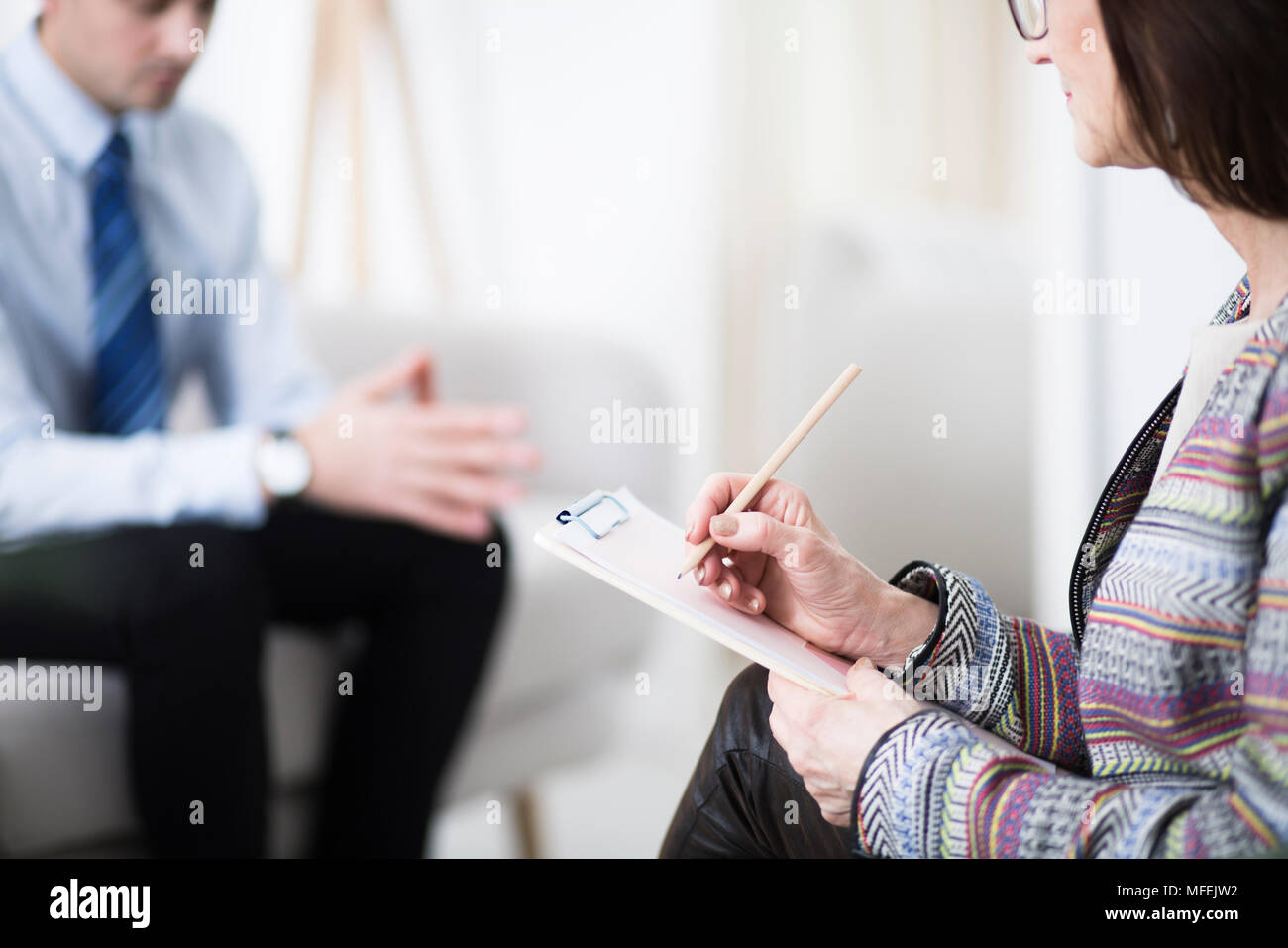 Elder therapist writing down notes during a conversation with her patient Stock Photo