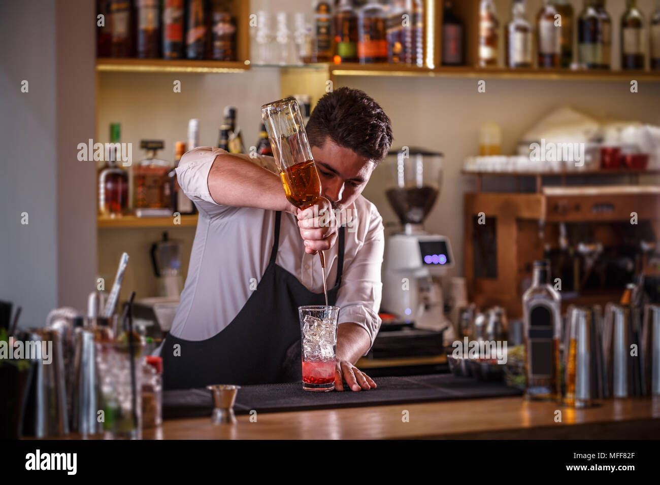 Barman pouring drink into a cocktail glass filled with ice cubes Stock Photo
