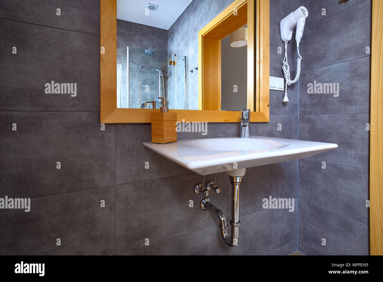 White shiny sink with mirror in bathroom with gray tile on walls. Interior of modern bath. Stock Photo