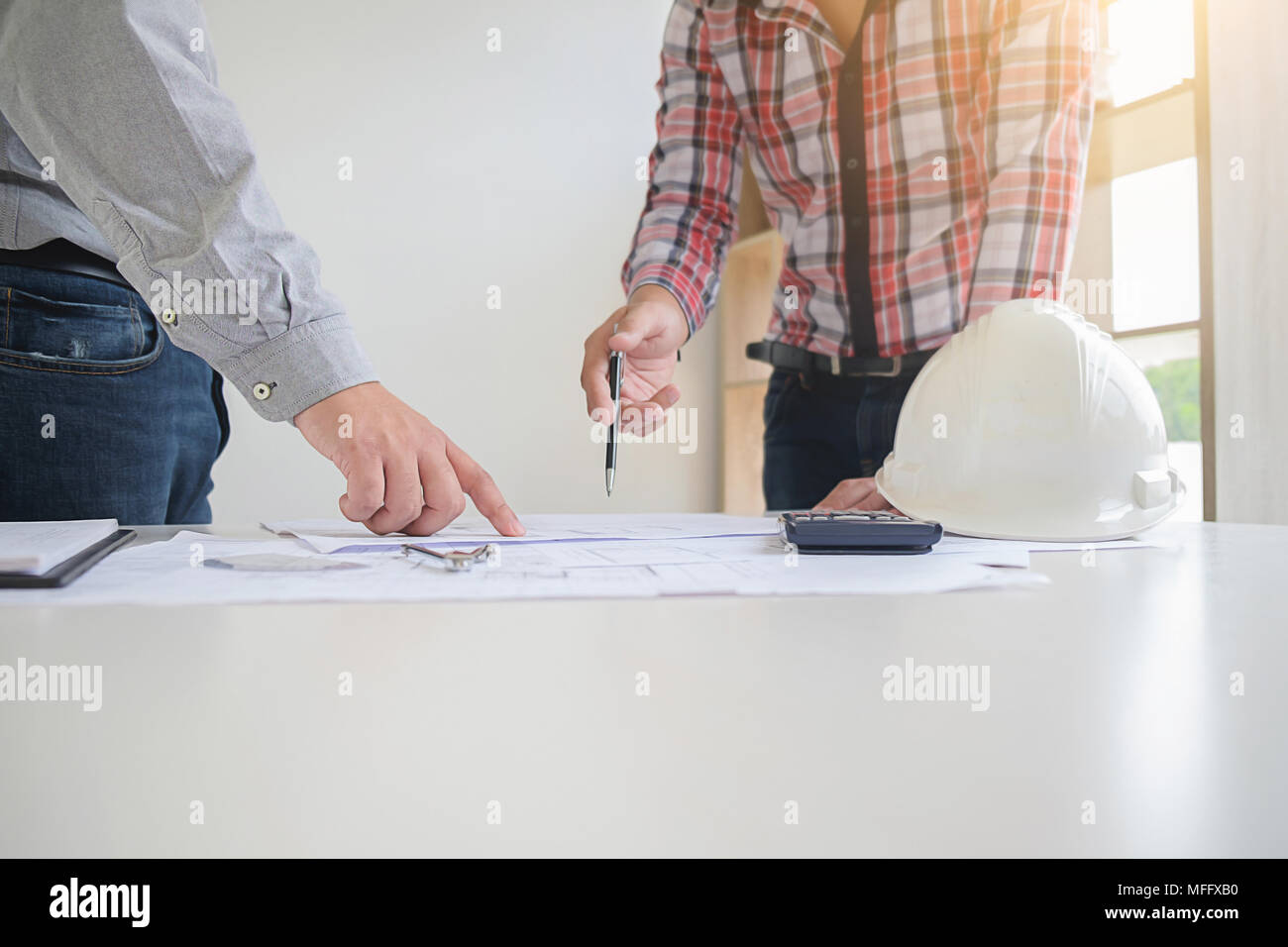 Engineers discuss a blueprint while checking information on a tablet computer in a office. Stock Photo