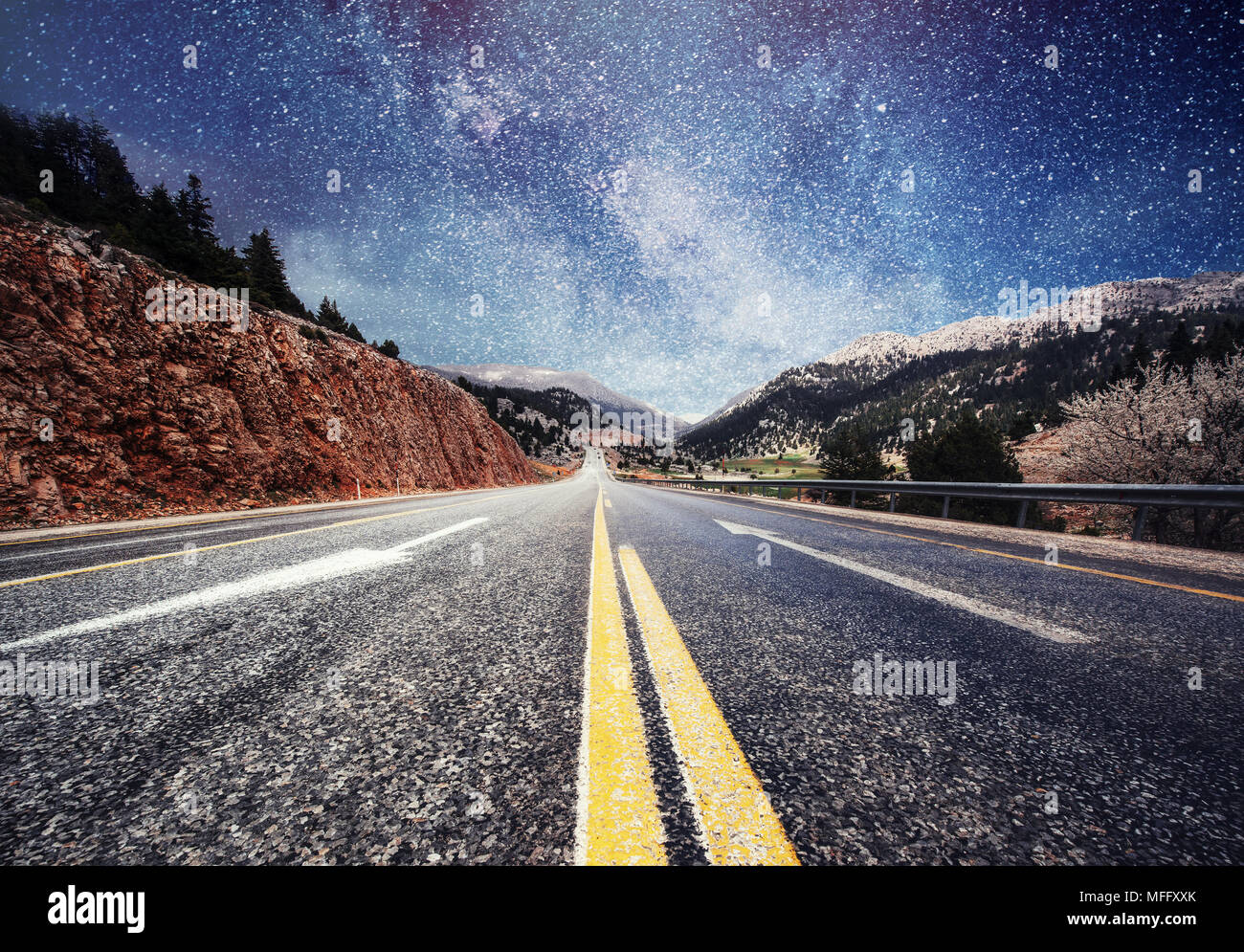 Asphalt road and lonely tree under a starry night sky and the Milky Way ...