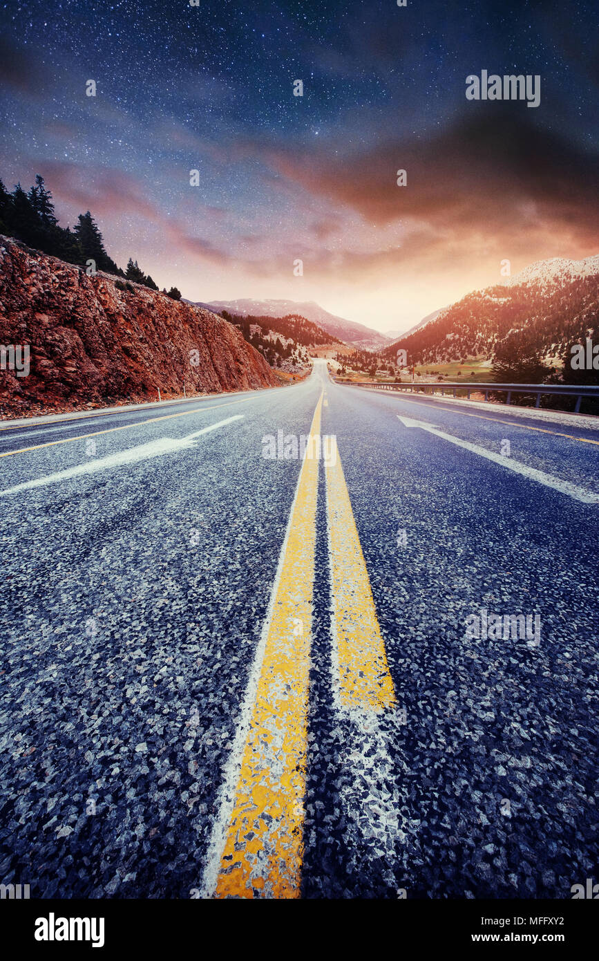 Asphalt road and lonely tree under a starry night sky and the Milky Way ...