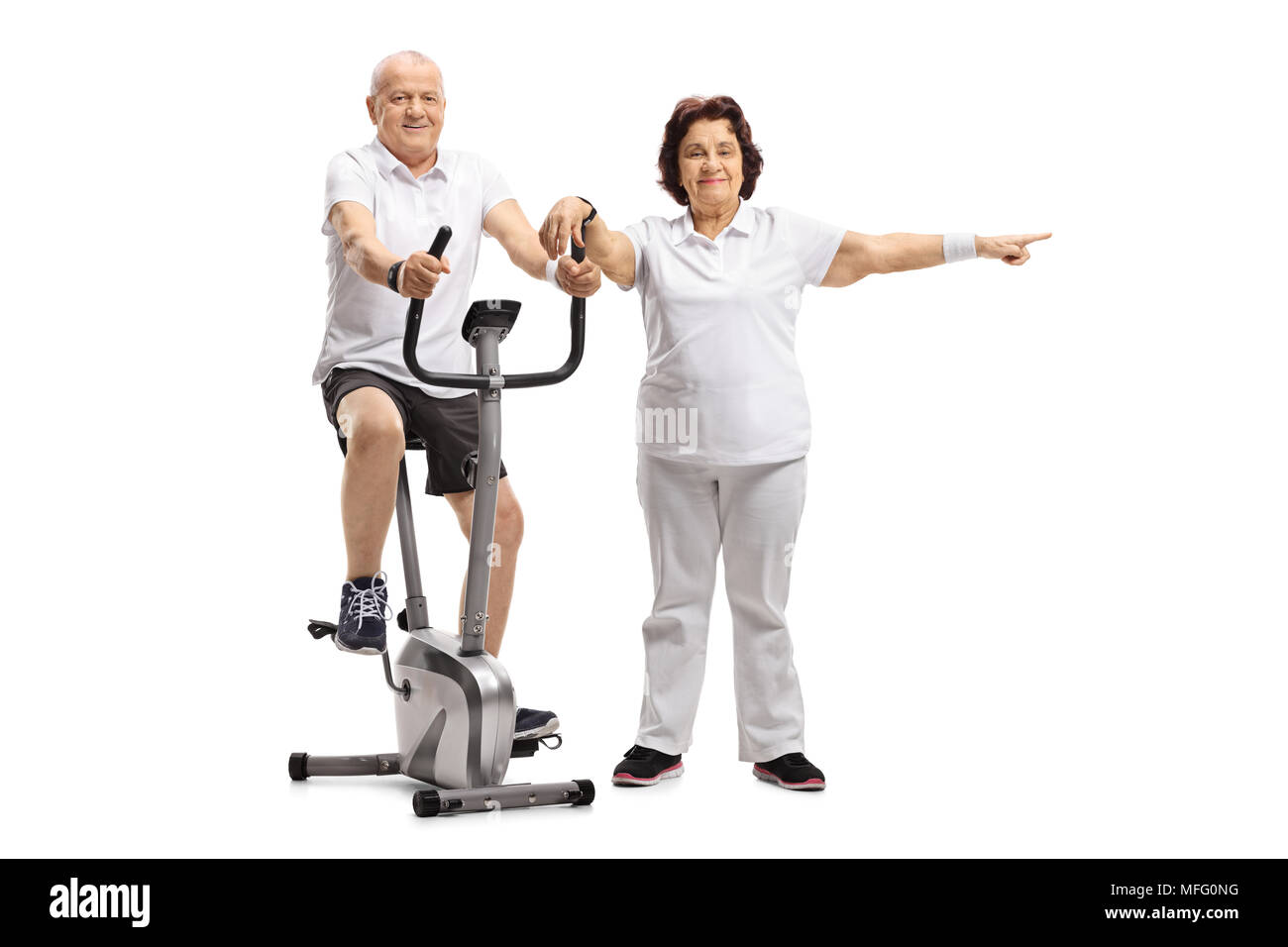 Mature man riding a stationary bike with a mature woman pointing isolated on white background Stock Photo