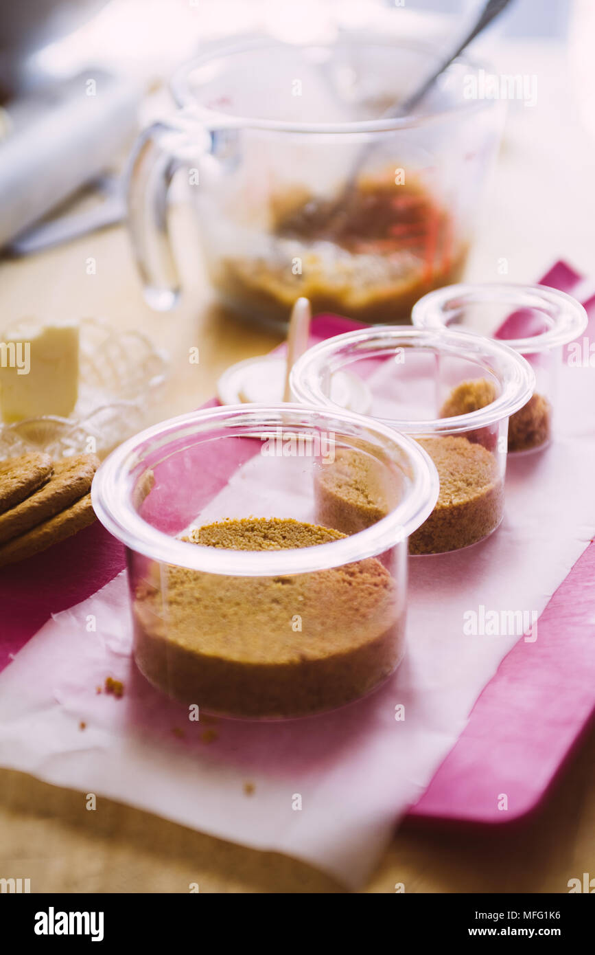 Plastic circular   cntainer are filled with granulated biscuits and butter then pressed to ccreate the base of chesecake dessert, cooking concept, ove Stock Photo